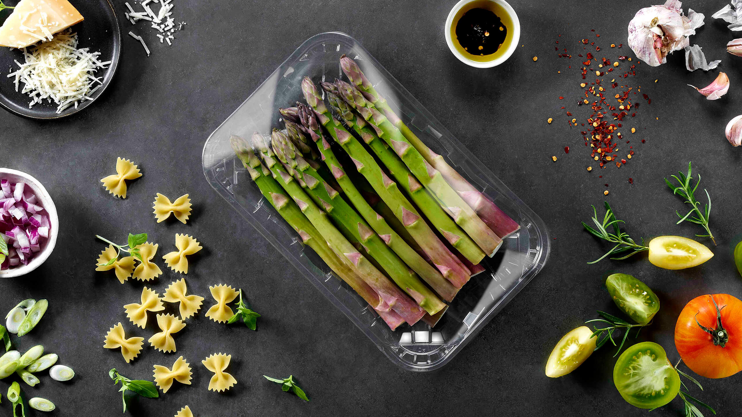 Auf einem Tisch liegen verschiedene Essenszutaten; in der Mitte liegt eine Kreislaufschale aus recycelten Kunststoff mit grünem Spargel.