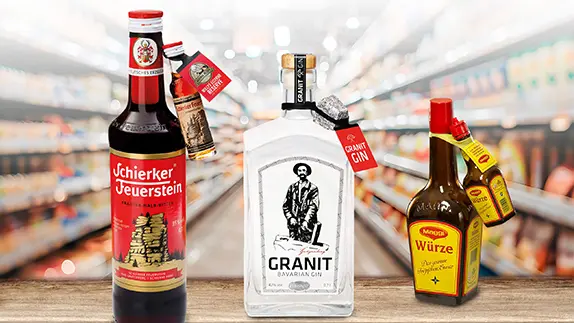 Im Vordergrund eines Einkaufsmarktes stehen 3 Flaschen mit Produktkennzeichnungen mit einem Elastitag