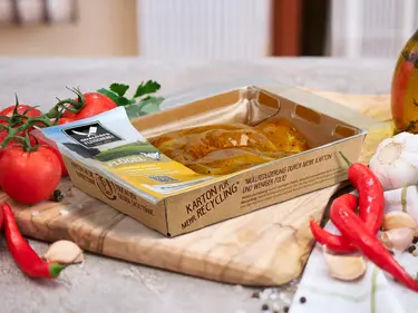 Auf einem Tisch liegen Zutaten wie Knoblauch und Tomaten sowie Fleisch in einer recycelten Verpackung