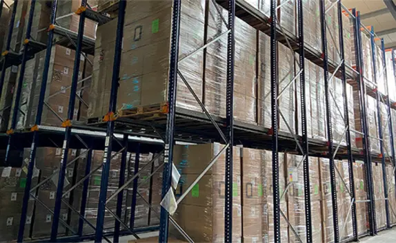 In einer Lagerhalle stehen in Regalen Paletten mit verpackten Waren.
