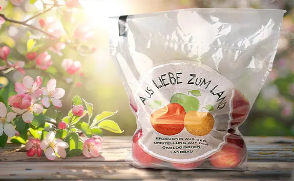 Auf einem Holztisch steht ein Kunststoffbeutel mit Zip-Verschluss und Äpfeln aus ökologischen Anbau